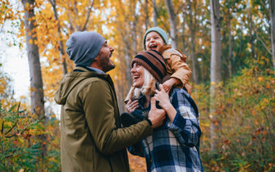 A family takes a walk in the fall woods with daughter on shoulders